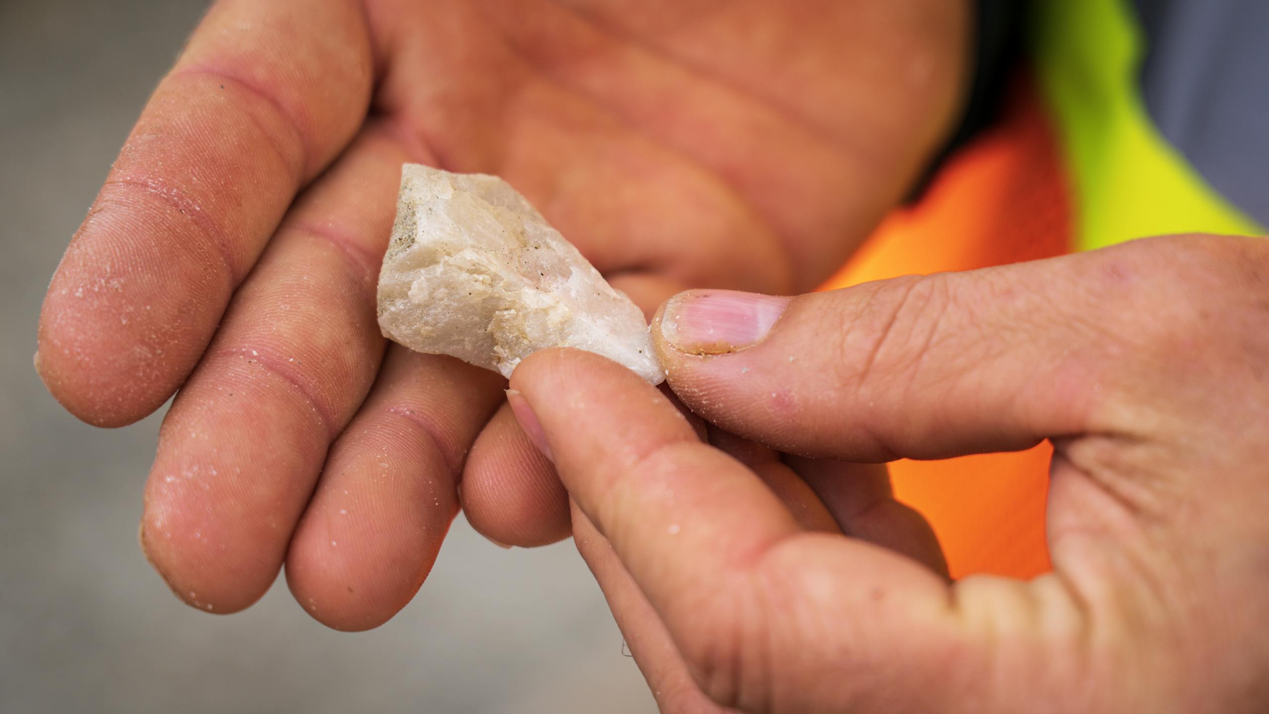 Detailed close-up of hands examining a white mineral stone outdoors.
